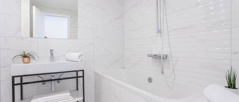 A modern bathroom with a white marble sink, a glass shower enclosure, and a built-in shelf with towels.