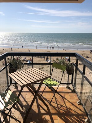Una terrazza con tavolo e sedie di legno, vista su una spiaggia con persone e cielo sereno.