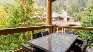 A covered outdoor area with a glass table and wicker chairs, overlooking a forested landscape.