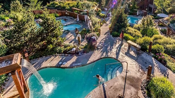Ein Resort mit mehreren Schwimmbecken, umgeben von üppiger Vegetation und Bergen im Hintergrund.