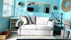 A room with a light-colored sofa, a ceiling fan, a large mirror, and a round woven wall hanging. - Beautifully renovated Gulf efficiency!  (North Redington Beach)