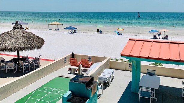 A beach view with a thatched umbrella, outdoor seating, and a green shuffleboard court. - Beautifully renovated Gulf efficiency!  (North Redington Beach)