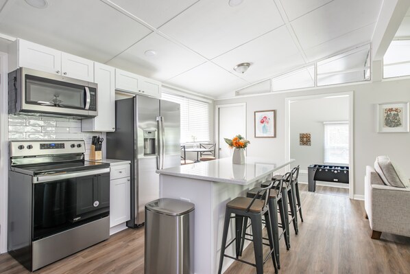 A modern kitchen with stainless steel appliances, a central island with bar stools, and a view to a dining area.