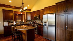 A kitchen with wooden cabinets, a stainless steel refrigerator, a microwave, and a granite countertop island with stools. - Mountain Views, Close to RMNP Entrance, Hot Tub! Casa Kiowa, Estes Park CO (Estes Park)