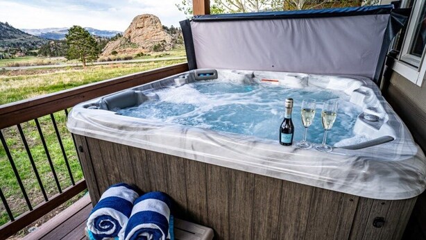 A hot tub with a view of mountains, a bottle of champagne, and two glasses on a wooden deck. - Mountain Views, Close to RMNP Entrance, Hot Tub! Casa Kiowa, Estes Park CO (Estes Park)