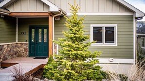 A house with a green exterior, a stone foundation, a green door, and a small evergreen tree in the front yard. - Mountain Views, Close to RMNP Entrance, Hot Tub! Casa Kiowa, Estes Park CO (Estes Park)