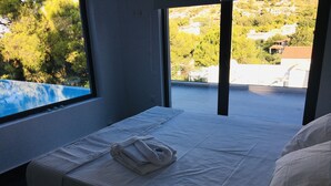 A hotel room with a bed, a window, and a view of a pool and greenery. - Villa   Tranquility. (Athens)