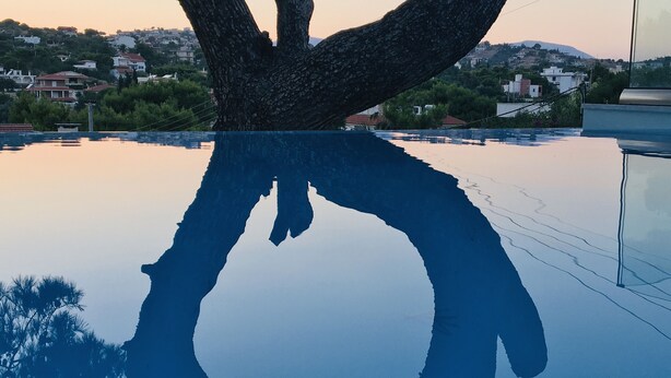 A pool with a tree silhouette reflection, surrounded by a residential area with houses and greenery. - Villa   Tranquility. (Athens)