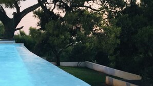 A swimming pool with a concrete edge, surrounded by grass and trees. - Villa   Tranquility. (Athens)
