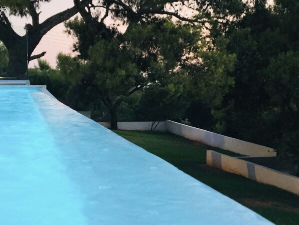 Una piscina con borde de hormigón, rodeada de césped y árboles.