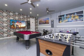 A room with a pool table, foosball table, and a painting of Las Vegas.