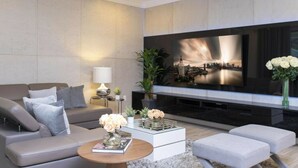 Un salon moderne doté d’un grand téléviseur à écran plat, d’un canapé, d’une table basse avec un livre et des fleurs, et d’une petite table d’appoint avec une lampe.