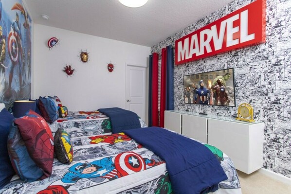 A bedroom with a Marvel-themed wall, a bed with superhero bedding, and a TV displaying Marvel characters.