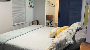 Ein Schlafzimmer mit einem Bett, Deckenventilator, einem Fenster mit Jalousien und einer Tür zu einem anderen Raum.