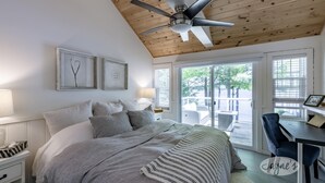 A bedroom with a bed, bedside tables, a desk, and a chair. There are two windows and a ceiling fan. - 5 Bed Cottage & 2 Bunkies! Boathouse Rooftop Deck with Sunsets! (Muskoka Lakes)