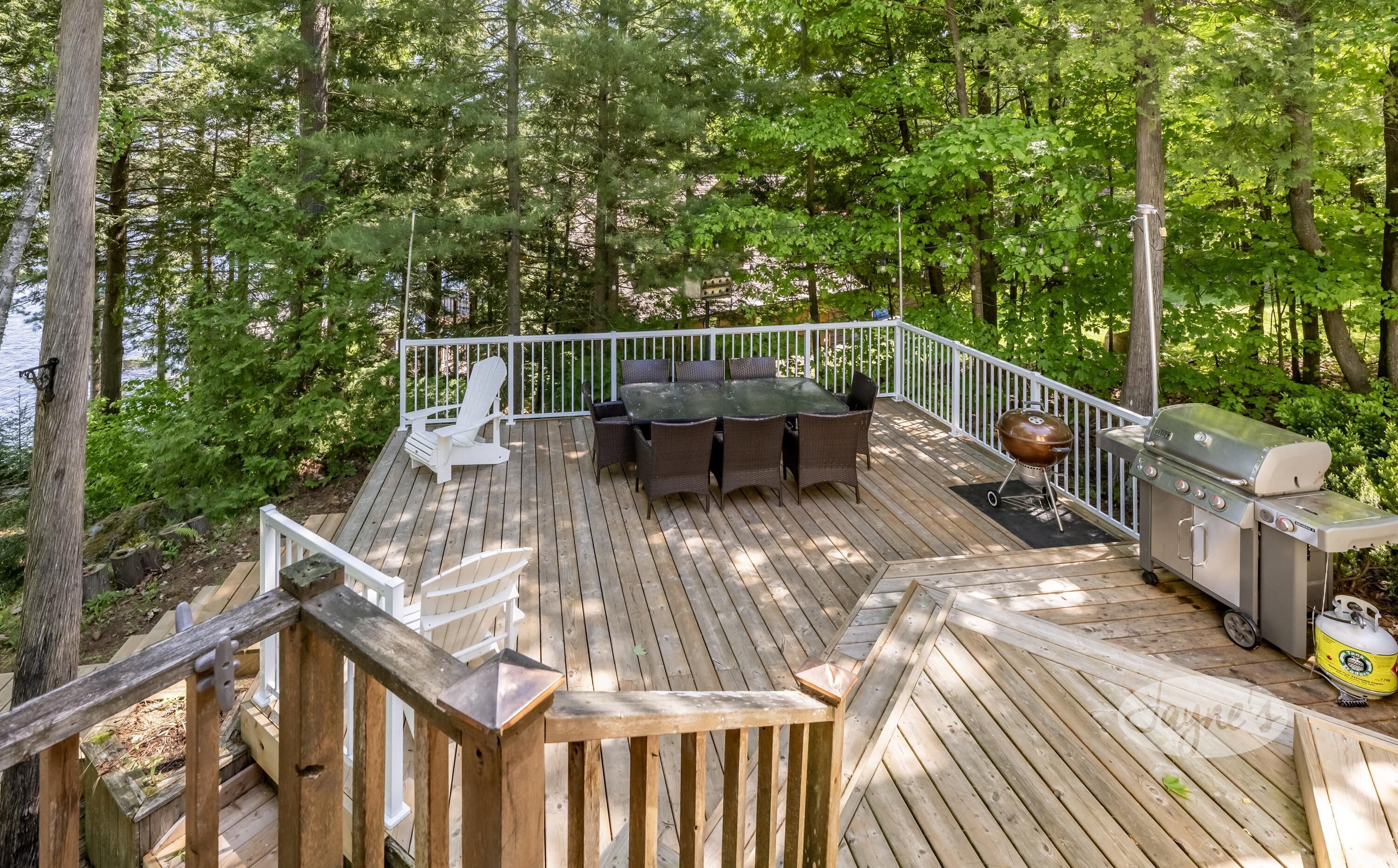 A wooden deck with a white railing, a table with chairs, and a grill.