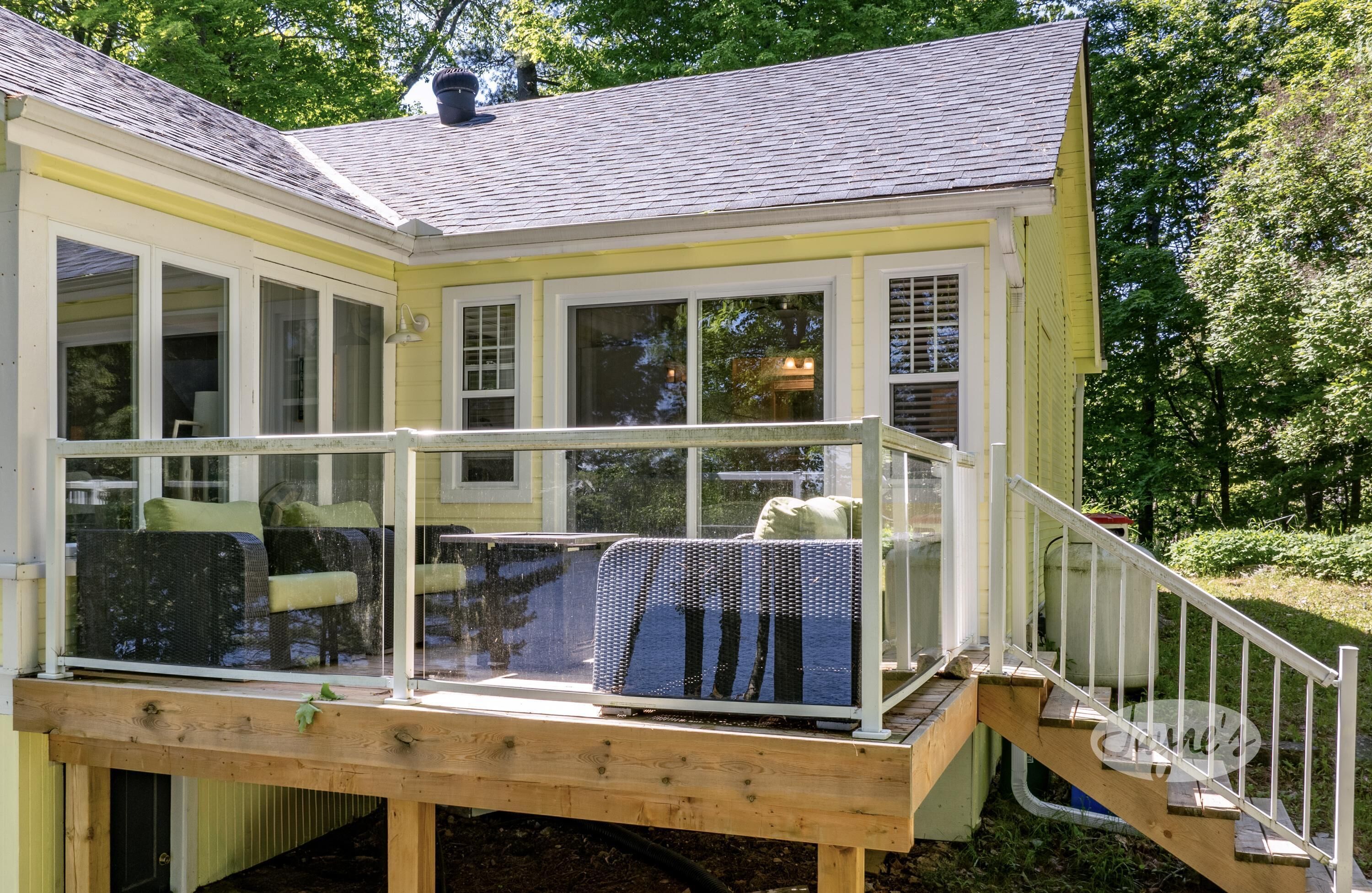Ein gelbes Haus mit überdachter Veranda, einer Holzterrasse und einer Treppe, die zum Eingang führt.