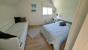 Una habitación pequeña y bien iluminada con dos camas individuales, una ventana con persianas, un radiador y una mesita con una lámpara.
