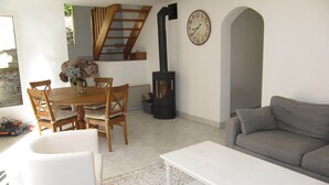 Una sala de estar con un sofá, una mesa de comedor con sillas, un reloj en la pared y una chimenea.