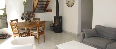A living room with a sofa, a dining table with chairs, a clock on the wall, and a fireplace.