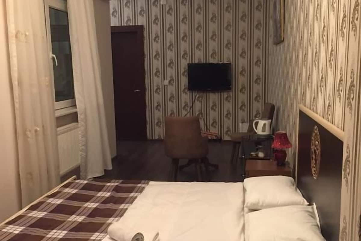 Une chambre d’hôtel avec un lit, une chaise, un bureau, une télévision et une fenêtre avec des rideaux.