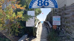 Una passerella in legno che conduce all'accesso pubblico alla spiaggia della Contea di Bay, con cartelli che segnalano pericoli e un divieto di accesso ai cani e agli animali domestici.