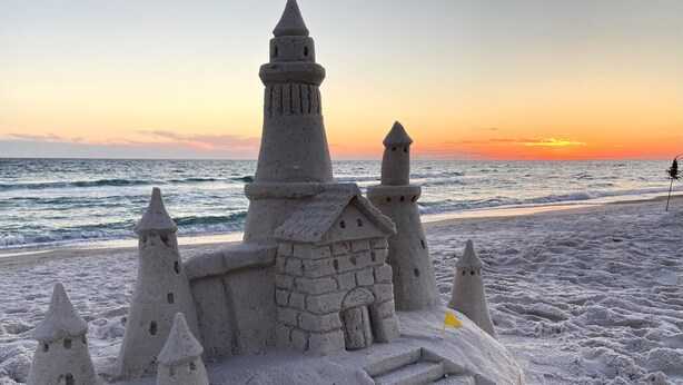 Un castello di sabbia con diverse torri e una bandiera su una spiaggia al tramonto.