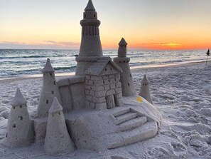 A sandcastle with multiple towers and a flag on a beach at sunset.