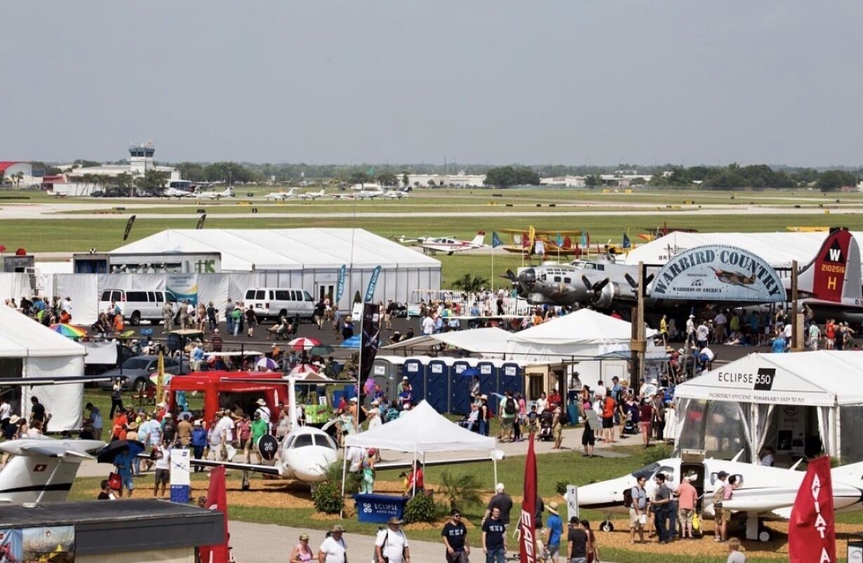 An outdoor event with multiple tents, a large crowd, and various aircraft on display.