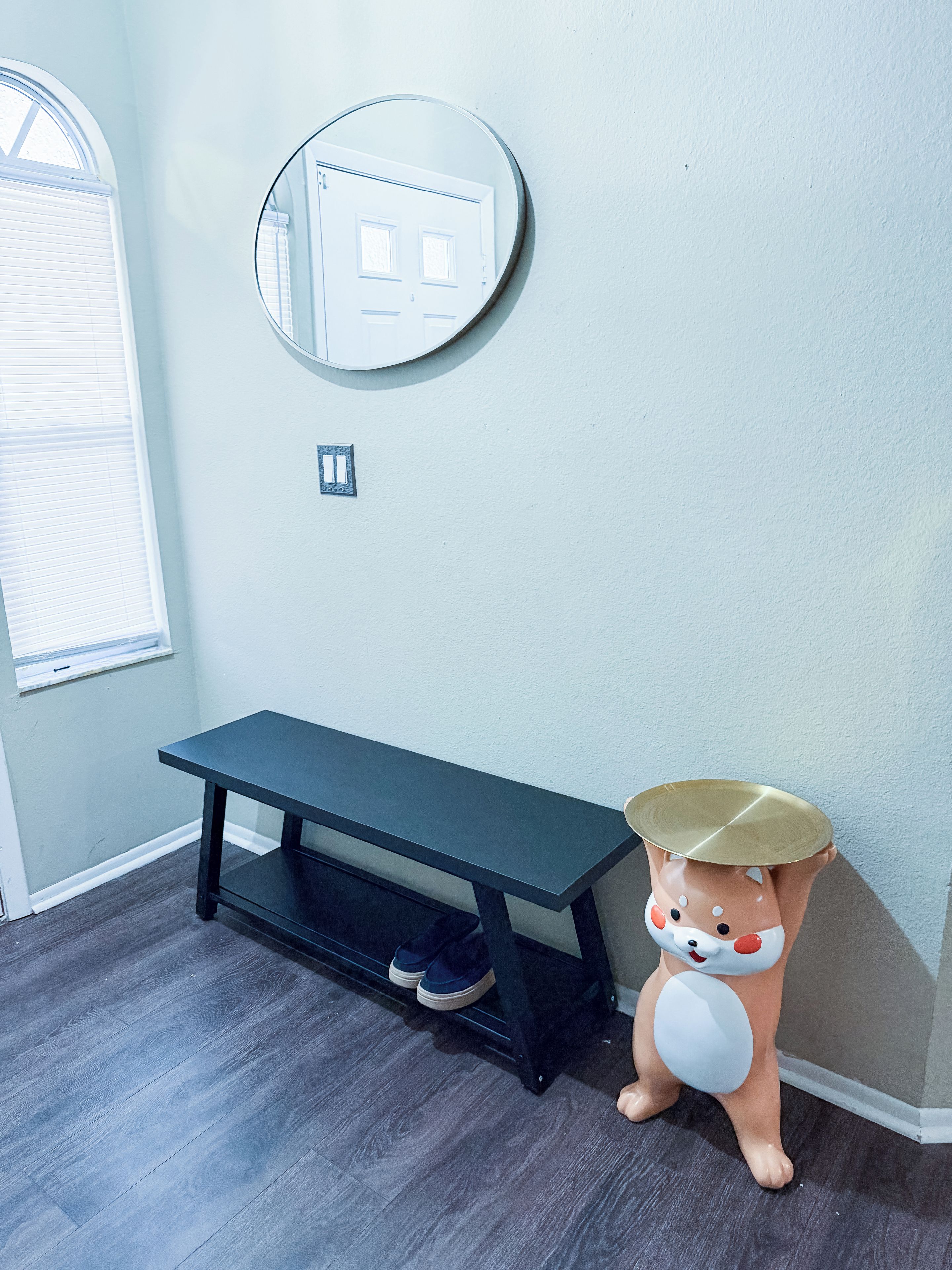 A room with a dark wooden bench, a round mirror on the wall, and a ceramic dog figurine.