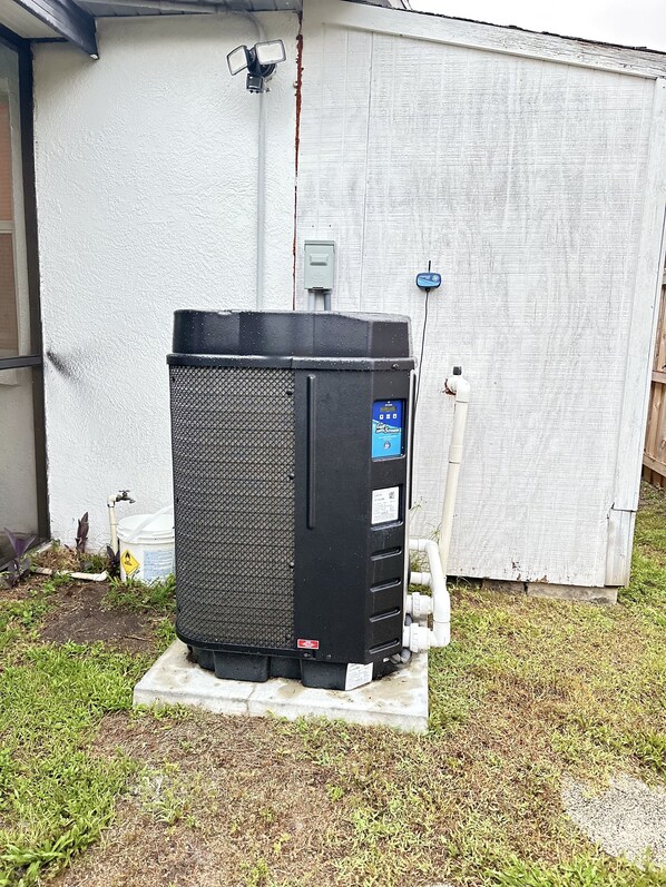 A large, black outdoor unit with a control panel, connected to a white building with a white exterior wall and a grey roof. - Paradise pool home (Plant City)