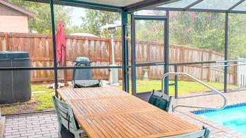 A covered patio with a wooden table and chairs, a pool, and a fenced backyard.