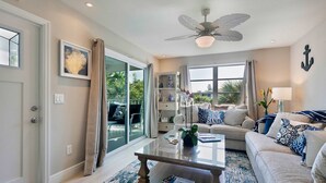 A modern living room with a glass door leading to a balcony, a ceiling fan, and a sofa with decorative pillows.