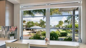 Una cocina con un gran ventanal con vistas a un paisaje tropical, una mesa blanca y sillas.