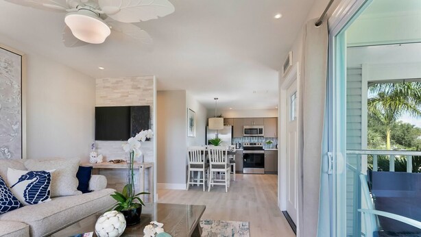 Una sala de estar moderna con sofá, mesa de centro y elementos decorativos. Se ve una cocina al fondo con un área de comedor.