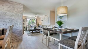 Un comedor con una mesa de madera, sillas blancas y una lámpara colgante.