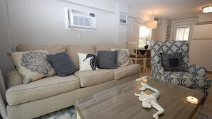 Una sala de estar con un sofá color beige, cojines estampados, una mesa de centro de cristal con un adorno, y un sillón con diseño.
