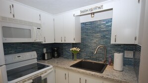 Una cocina con gabinetes blancos, un lavamanos de acero inoxidable, un microondas, una estufa y una cafetera.