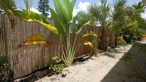 Un jardín con cerca de bambú, diversas plantas tropicales y un camino de grava.