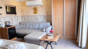 A hotel room with a sofa, a small table with a vase of flowers, a coffee maker, and a TV mounted on the wall.