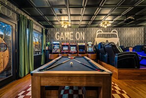 A pool table with a neon sign, arcade machines, and a lounge area with a pool table.