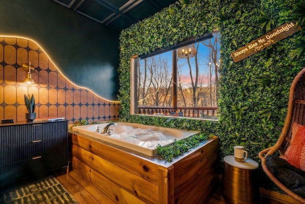 A bathroom with a wooden bathtub, a window with a view, and a sign that says 'Always Kiss Me Goodnight.'
