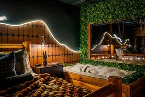 A modern bathroom with a wooden vanity, a large mirror, and a bathtub surrounded by greenery.