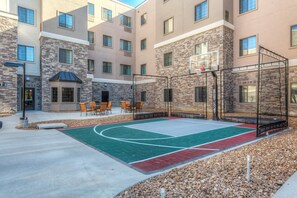 Ein Basketballplatz im Freien mit Netz, umgeben von Gebäuden aus Stein und Backstein, sowie Sitzmöglichkeiten im Freien.