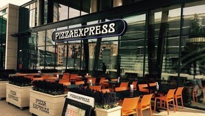 Een terras van een pizzeria met een grote glazen gevel en een bord waarop 