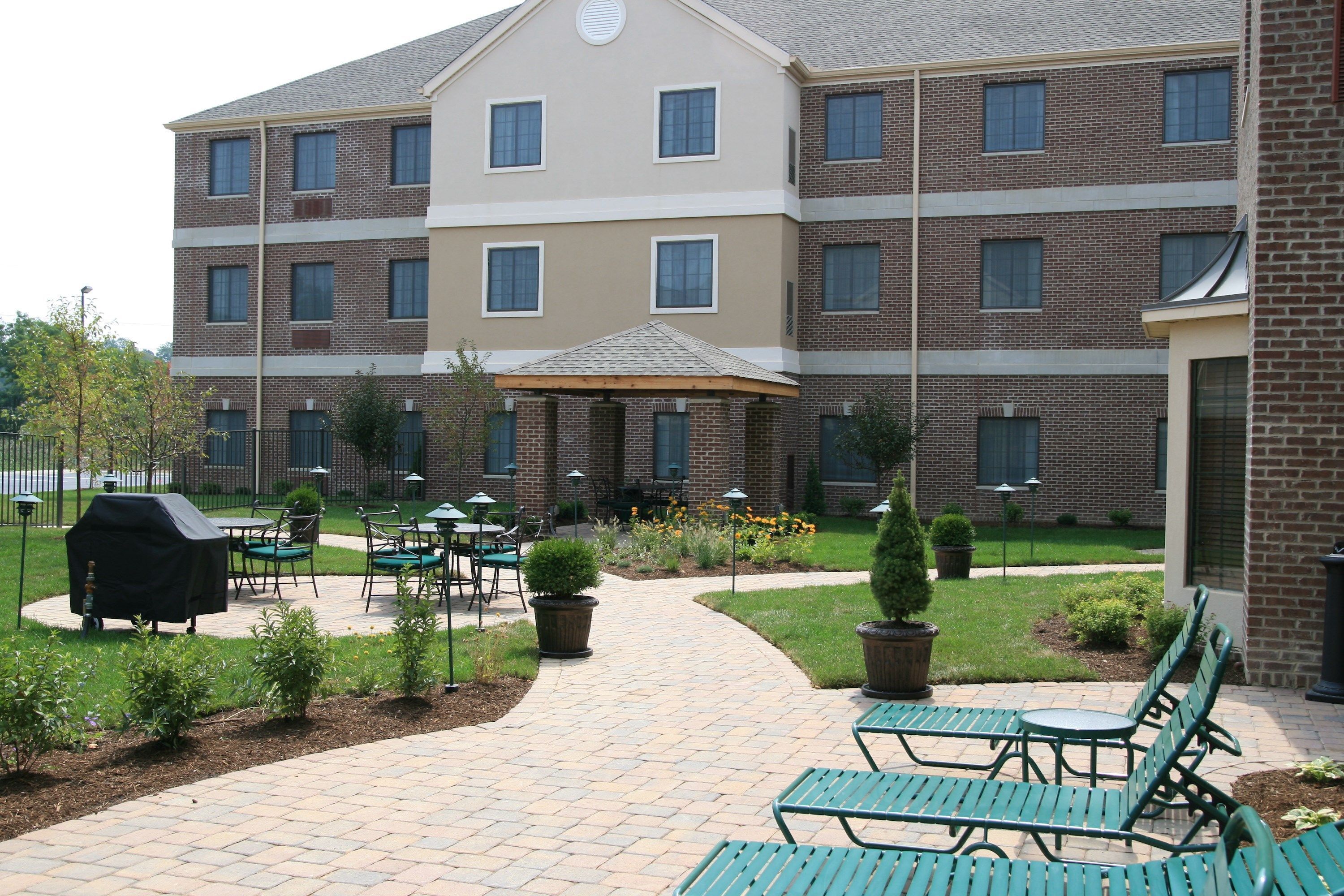 A multi-story building with a brick facade, outdoor seating area with tables and chairs, and a paved walkway.