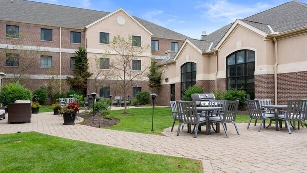A courtyard with outdoor seating, a barbecue grill, and a brick building with multiple windows.