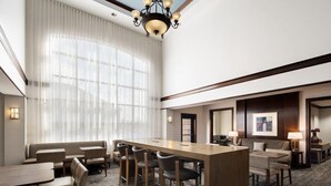 A hotel room with a large window, a long table with chairs, a sofa, and a lamp.