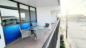 Ein Balkon mit Korbmöbeln und einem Glastisch, mit Blick auf eine Straße mit Autos und Gebäuden.