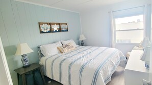 Ein Schlafzimmer mit einem Bett, zwei Nachttischen mit Lampen, einem Fenster mit Vorhängen und Wanddekoration.